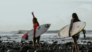 Surfer girls carrying boards across the rocks in El Tunco, El Salvador