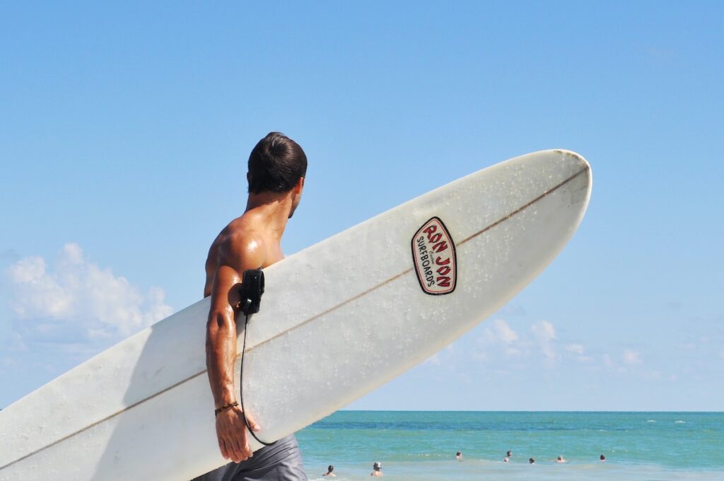 Man carrying a longboard surfboard on the beach