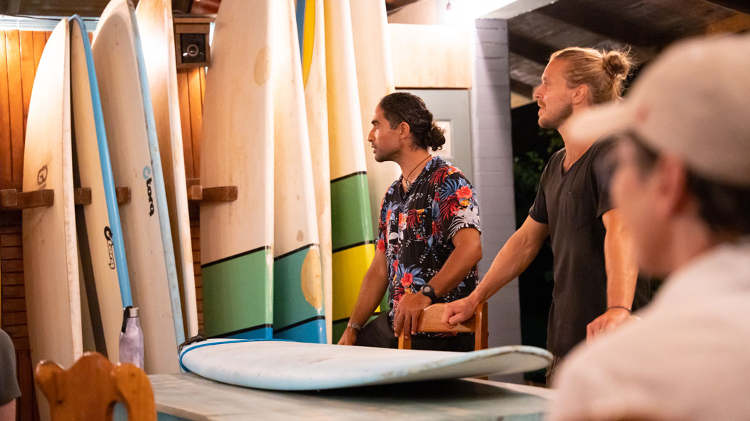 Surf coaches explaining parts of surfboard to beginner surfers during the first theory class of the week.