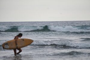Woman holding an epoxy surfboard on the beach with stormy waves