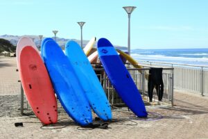 stack of colorful foam surfboards leaning against a metal fence near the ocean