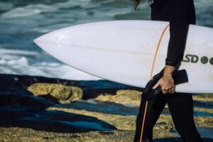 surfer wearing a wetsuit carrying a white shortboard under his arm
