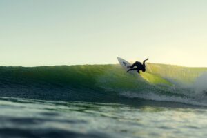 Surfer riding a PU board on a right hand wave with light shining through