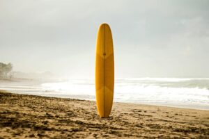A single yellow longboard propped up in the sand in front of the ocean