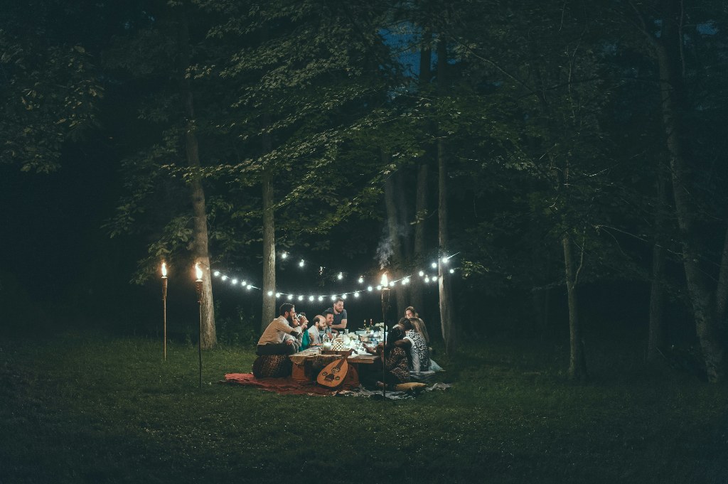 Group of friends camping and enjoying a meal under string lights